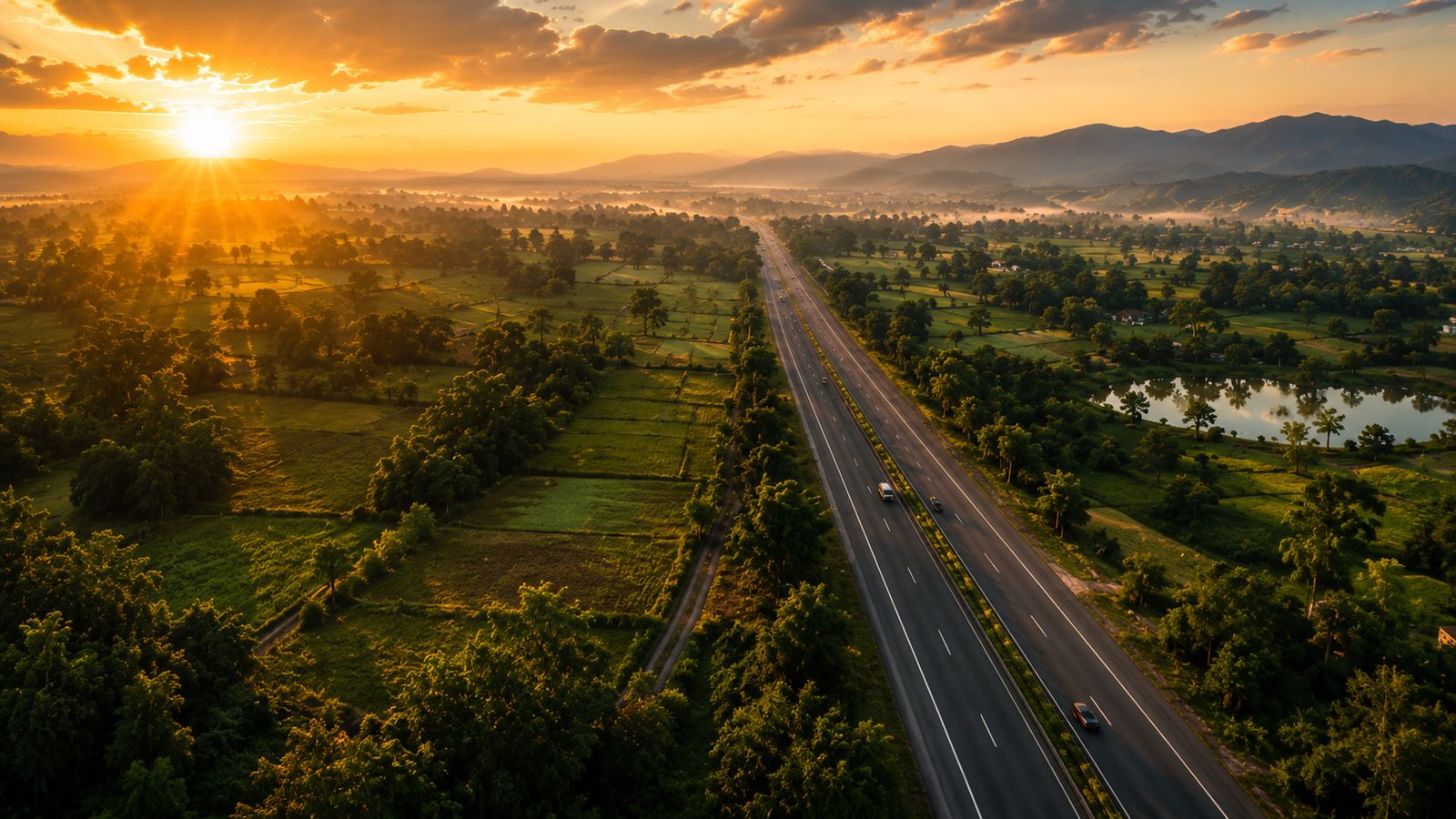 Aerial golden-hour view of the NH731 highway winding through lush green farmland valleys with misty mountains